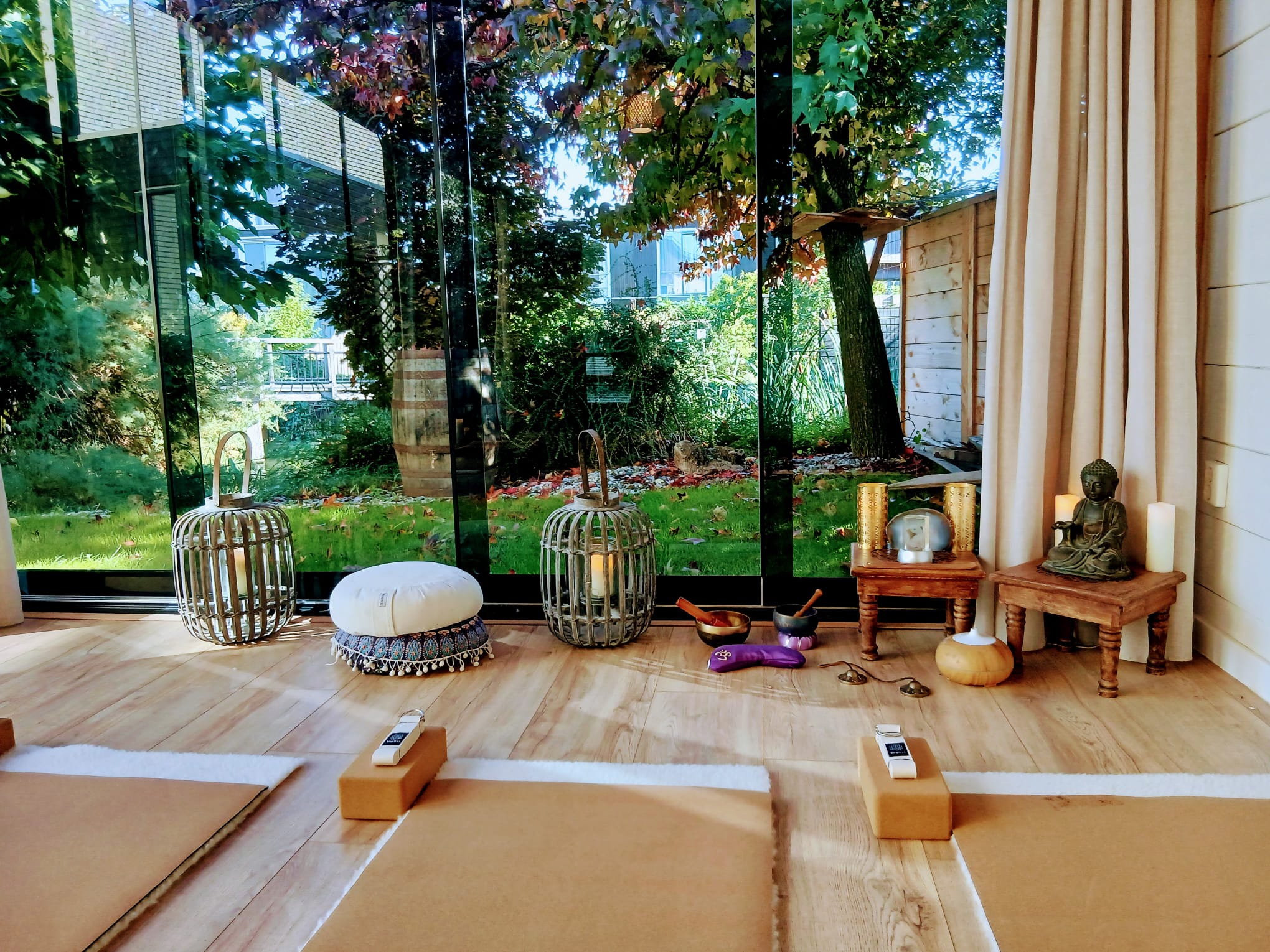 Yogastudio van SensZenjoy met meditatiekussens, klankschalen en lantaarns voor de glazen pui met uitzicht op de tuin